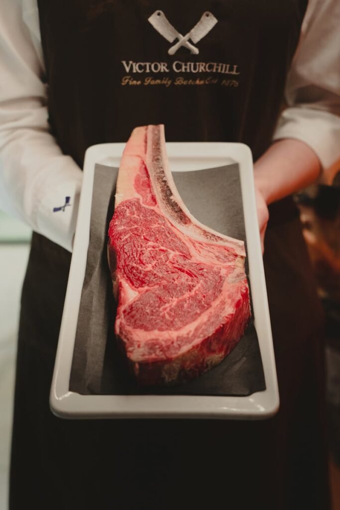 Close-up of butcher presenting a marbled beef steak on a tray, ready for cooking.