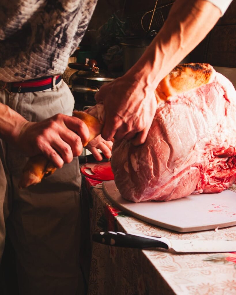 Carnicería Botía en Córdoba Man using a knife to butcher a large piece of meat in an indoor kitchen setting.