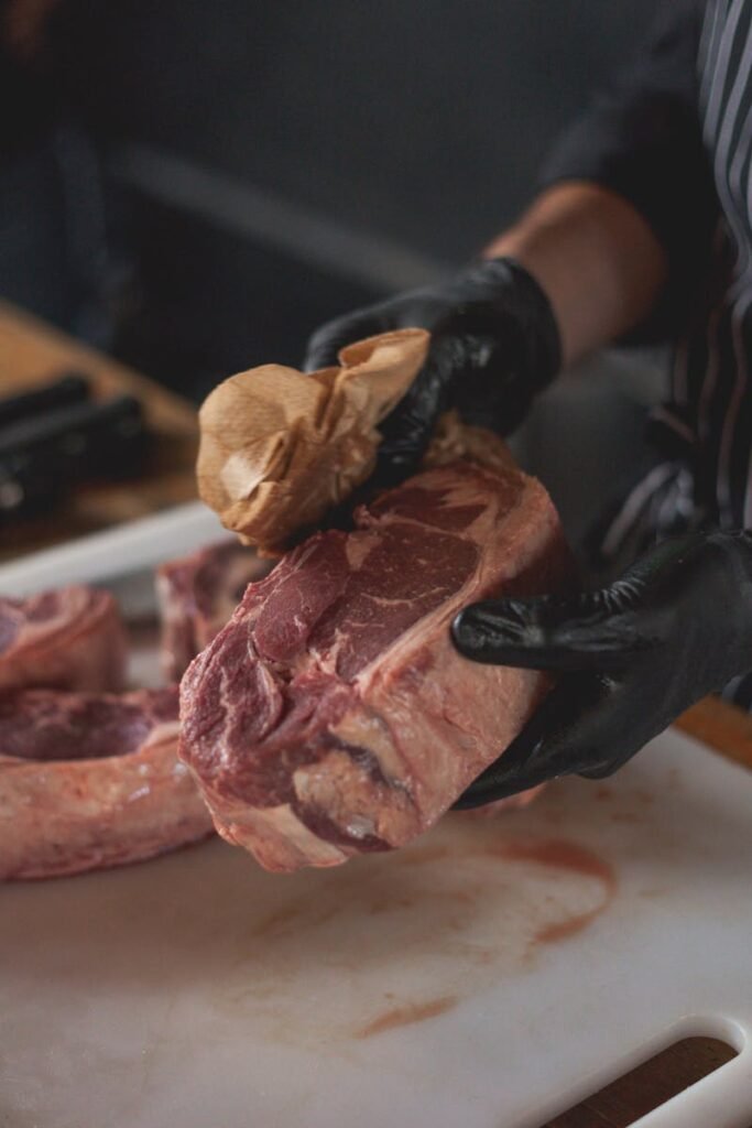 Close-up of a chef wiping fresh raw beef steak with paper towel on a chopping board.