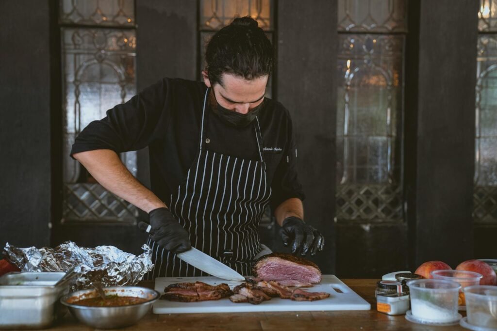 Chef preparing and slicing meat on cutting board indoors with precision and focus.