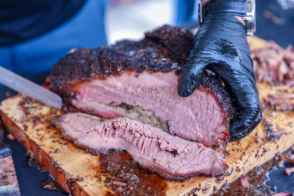 Deliciously smoked brisket being sliced with gloves on a wooden board.